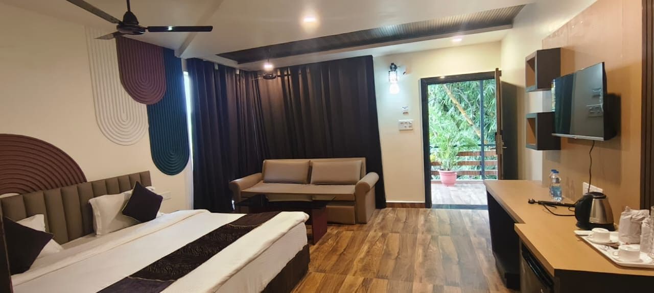 A hotel room with a bed, a sofa, a desk with a TV, and a view of the outdoors.