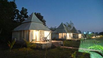 A row of small, lighted cottages with conical roofs, each with a seating area and a pathway leading to the entrance.