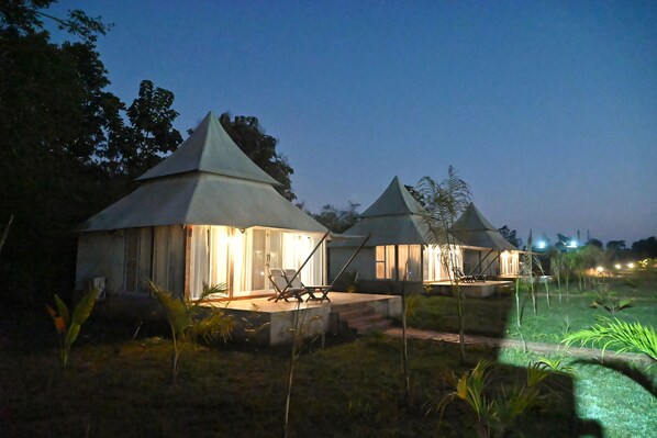 A row of small, lighted cottages with conical roofs, each with a seating area and a pathway leading to the entrance.
