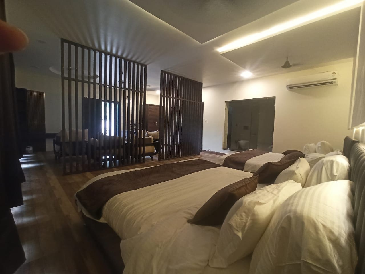 A hotel room with a large bed, a seating area with chairs, and a partition with vertical bars.