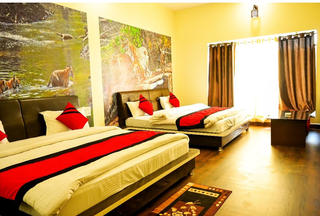 Une chambre d’hôtel avec deux lits, chacun agrémenté de draps rouges et blancs, une grande peinture représentant un paysage fluvial et une fenêtre avec des rideaux.