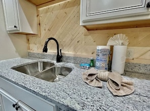 A kitchen with a granite countertop, stainless steel sink, and wooden wall paneling. - Bearly Behavin | Hot Tub Pool Table Great Location (Sevierville)