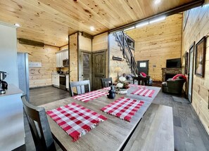 A wooden interior with a dining table set with red and white checkered placemats, a staircase, and a kitchen area. - Bearly Behavin | Hot Tub Pool Table Great Location (Sevierville)