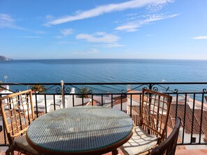 A balcony with a round table and chairs, overlooking a coastal view. - Apartment in Nerja Near Carabeillo Beach (Nerja)