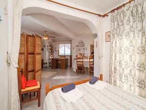 A bedroom with a bed, two chairs, a wooden table, and a view of the dining area. - Apartment in Nerja Near Carabeillo Beach (Nerja)