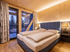 Ein Schlafzimmer mit einem großen Bett, Holzwänden und Blick auf Bäume durch eine Glastür.