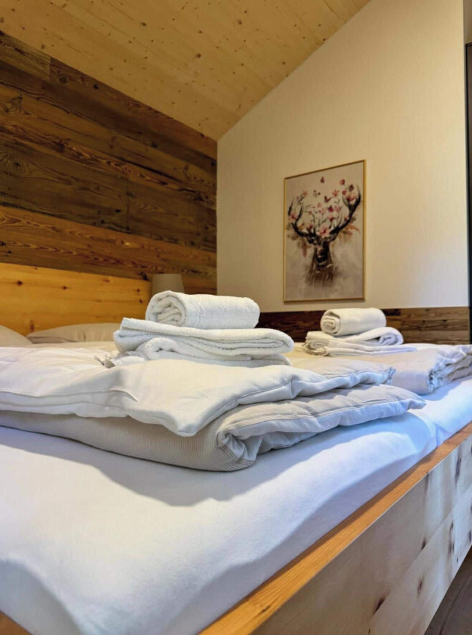 Une chambre d’hôtel avec une tête de lit en bois, un lit recouvert de serviettes blanches soigneusement pliées, et un tableau représentant un arbre aux fleurs roses accroché au mur.