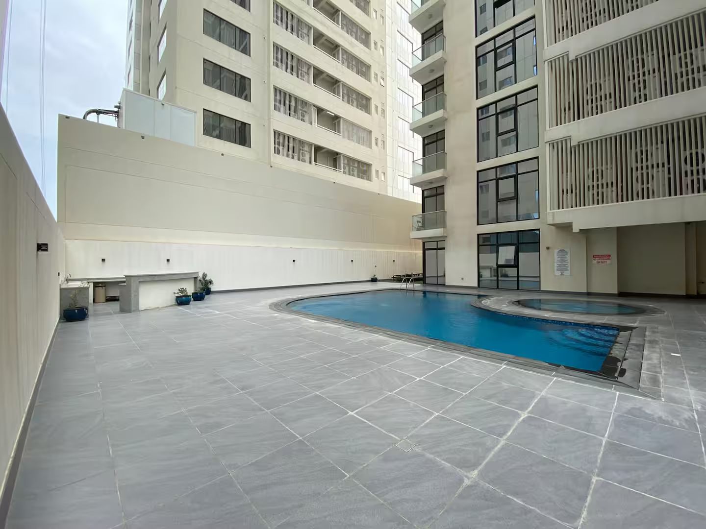 A swimming pool area with a flat roof and a building with multiple balconies in the background.