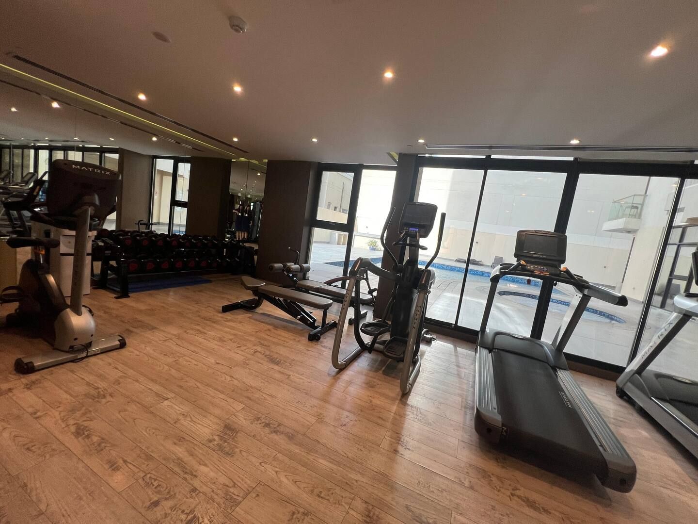 A gym with cardio machines, dumbbells, and a view of a swimming pool through large windows.