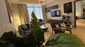 A modern living room with a sofa, coffee table, and dining area. A flat-screen TV is mounted on the wall. - Stylish Downtown & Close to Attractions F97O (Manama)