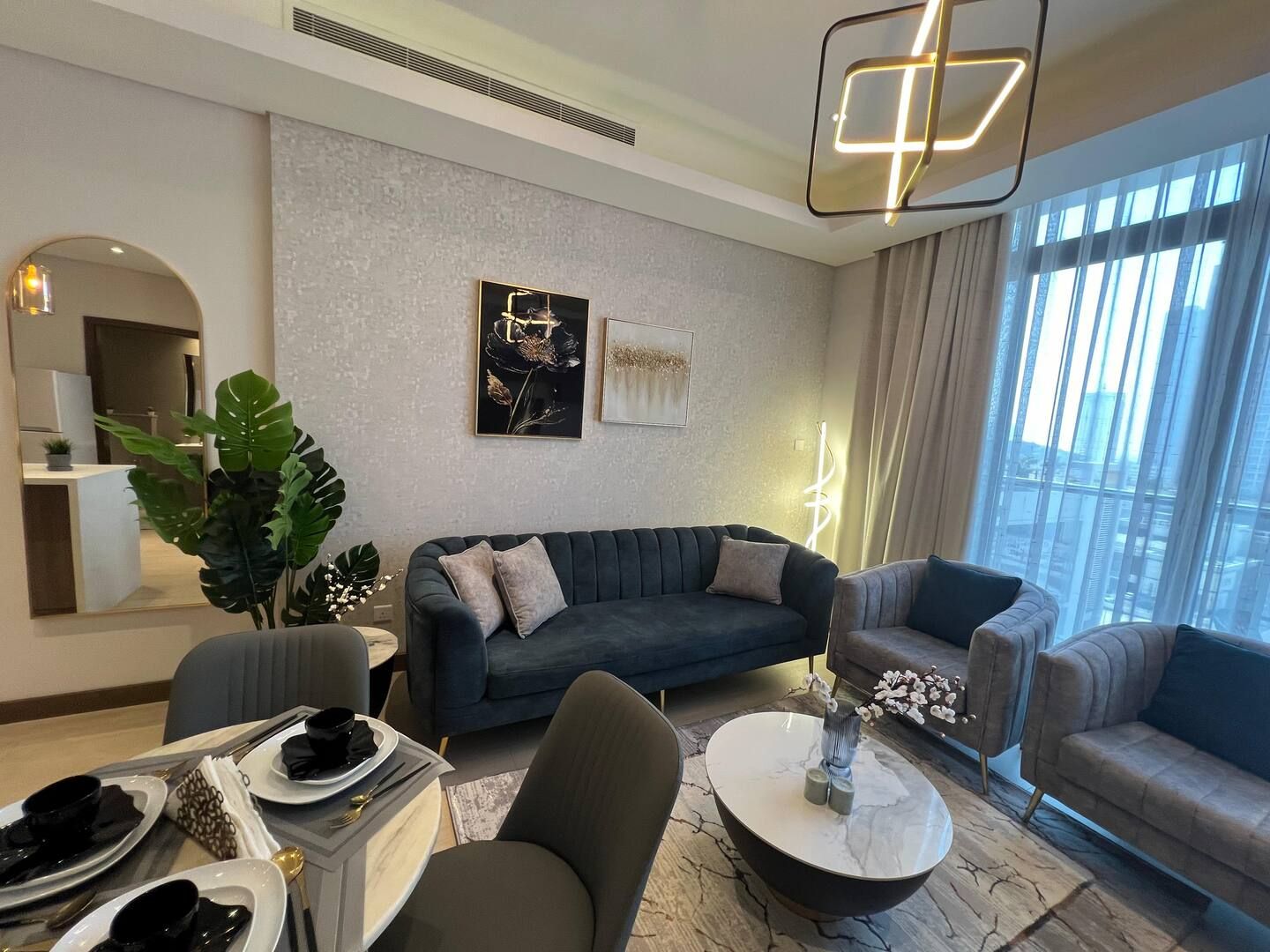 A modern living room with a sofa, armchairs, a coffee table, and a dining area with plates and cutlery.