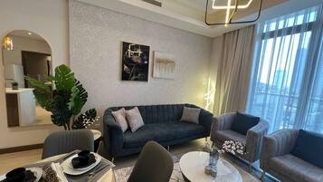 A modern living room with a sofa, armchairs, a coffee table, and a dining area with plates and cutlery.