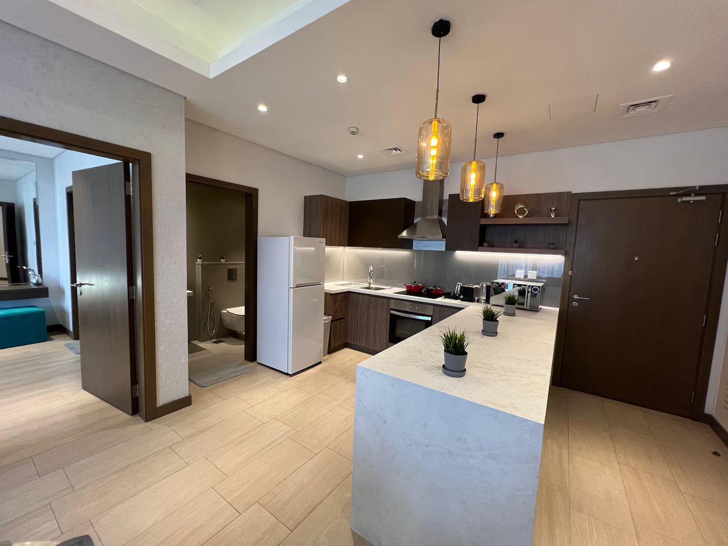 A modern kitchen with a central island, built-in appliances, pendant lighting, and a view into the adjacent bathroom.