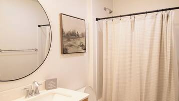 Une salle de bain avec un meuble-lavabo en bois, des toilettes, un rideau de douche et un miroir fixé au mur.