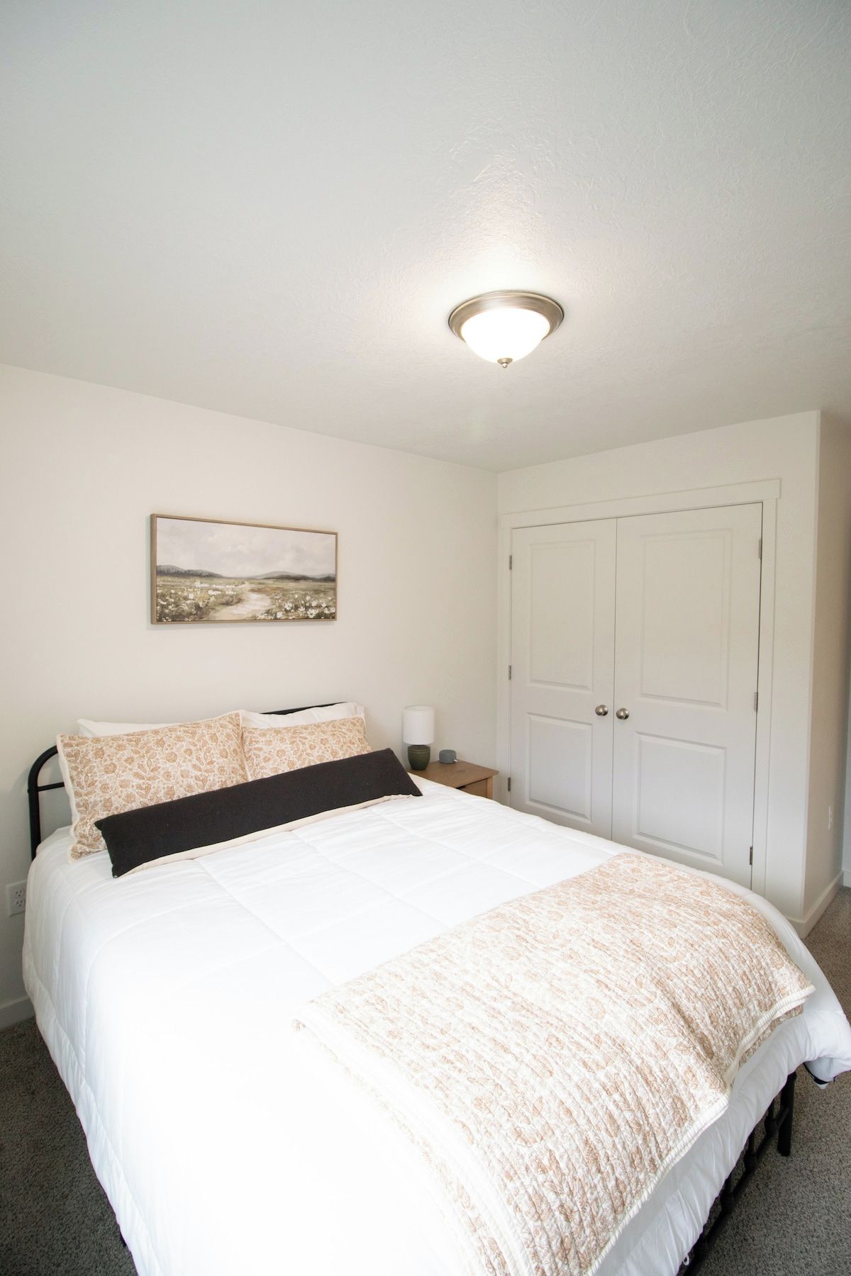 A bedroom with a bed, a nightstand, a lamp, a door, and a painting on the wall.