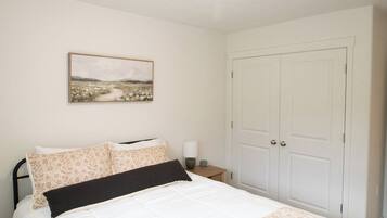 A bedroom with a bed, a nightstand, a lamp, a door, and a painting on the wall.