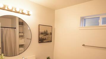 Une salle de bain comprenant un meuble-lavabo, des toilettes, un rideau de douche, un porte-serviettes, une fenêtre et un tableau accroché au mur.