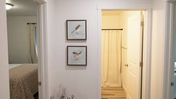A hallway with a bed, a door, and two framed pictures on the wall.