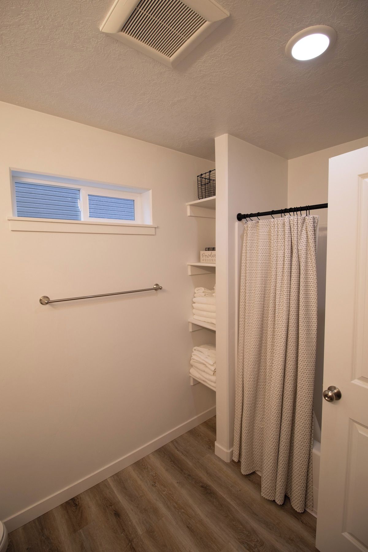 A bathroom with a shower curtain, a towel rack, and a window with blinds.