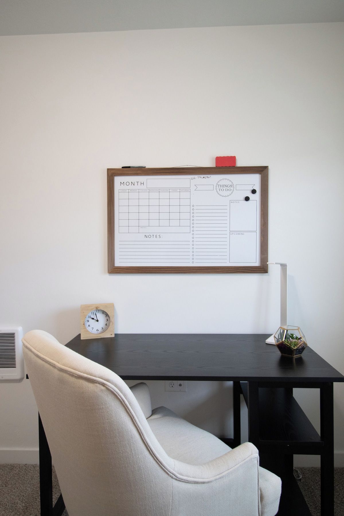 A desk with a whiteboard, a clock, and a chair.