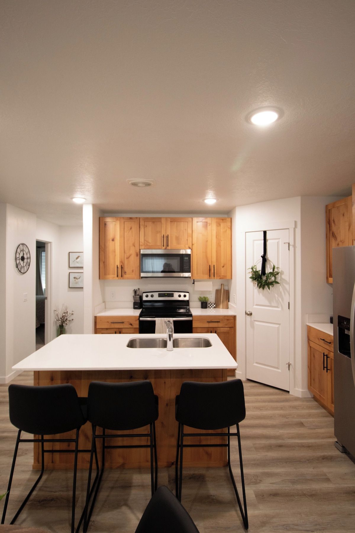 A modern kitchen with wooden cabinets, a central island with bar stools, stainless steel appliances, and recessed ceiling lighting.