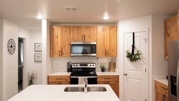 A modern kitchen with wooden cabinets, a central island with bar stools, stainless steel appliances, and recessed ceiling lighting.