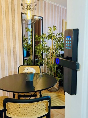 A dining area with a round table, chairs, a potted plant, and a wall-mounted electronic device. - El mejor lugar - Hospital UC - Metro (Santiago)