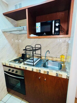 A compact kitchen with a microwave, stove, oven, and sink. - El mejor lugar - Hospital UC - Metro (Santiago)