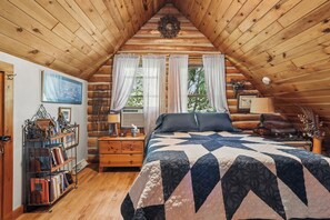 A log cabin bedroom with a wooden ceiling, a bed with a quilt, a nightstand, a lamp, a bookshelf, and a window with curtains. - 3-bedroom log cabin in tranquil Sturgeon Bay close to Lake Michigan (Sturgeon Bay)