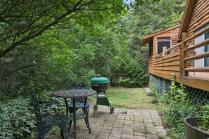 Eine Terrasse mit einem runden Metalltisch und Stühlen, einem grünen Grill und einer Holzhütte.