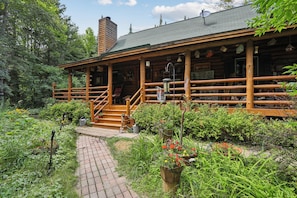 A wooden lodge with a covered porch, a brick pathway leading to the entrance, and a garden with various plants and flowers. - 3-bedroom log cabin in tranquil Sturgeon Bay close to Lake Michigan (Sturgeon Bay)