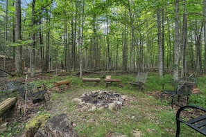 A forested campsite with a fire pit, benches, and metal chairs. - 3-bedroom log cabin in tranquil Sturgeon Bay close to Lake Michigan (Sturgeon Bay)