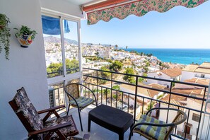 A balcony with wicker furniture, a view of a coastal town, and a clear sky. - Apartment in Nerja Near Burriana Beach (Nerja)