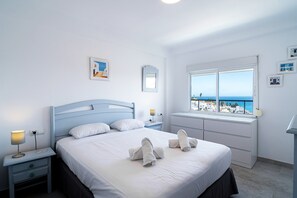 A bedroom with a bed, bedside tables, a lamp, a window with a view of the sea, and a wall with framed pictures. - Apartment in Nerja Near Burriana Beach (Nerja)