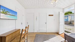 A room with a wooden bench, a rug, a painting of a beach, and a view of a building outside.