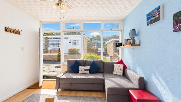 A modern living room with a grey sofa, a ceiling fan, and a view of the outside.