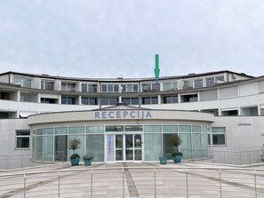 Ein Gebäude mit einem Schild, das 'RECEPCJA' zeigt, am Eingang, mit einer gewölbten Fassade, großen Fenstern und Topfpflanzen.