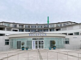 Un edificio con un letrero que dice 'RECEPCJA' en la entrada, con fachada curva, ventanas grandes y plantas en macetas.