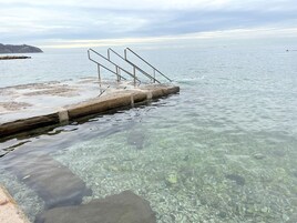 Un cuerpo de agua clara con un muelle de hormigón y barandillas de metal.