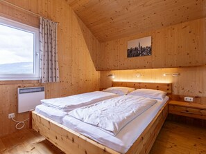 A wooden room with a bed, a nightstand, a wall-mounted light, and a window with curtains. - One-bedroom Cabin (Sankt Georgen am Kreischberg)