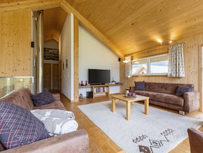Ein gemütliches Wohnzimmer mit Holzbalkendecke, einem Flachbildfernseher, einer Couch und einem Couchtisch.