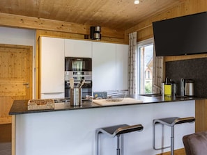 Eine moderne Küche mit einer zentralen Kochinsel, Barhocker, einem Backofen und einem Fenster mit Vorhängen.