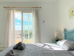 Ein Schlafzimmer mit einem Bett, einem Nachttisch, einer Lampe und Blick ins Freie.