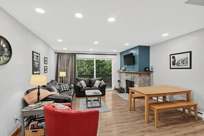 A modern living room with a sofa, red chair, wooden table, fireplace, and a TV mounted on the wall. - Alyeska Mountain Getaway | Adventure & Relaxation (Anchorage)