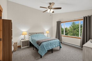 A bedroom with a bed, two bedside lamps, a ceiling fan, a window with curtains, and a view of trees. - Alyeska Mountain Getaway | Adventure & Relaxation (Anchorage)