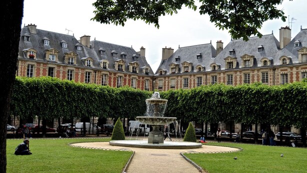 A courtyard with a fountain, surrounded by a hedge and a building with multiple windows and chimneys. - JUST STEPS FROM THE HISTORIC PLACE DES VOSGES, CENTRE POMPIDOU – 6 BEDROOM (Paris)