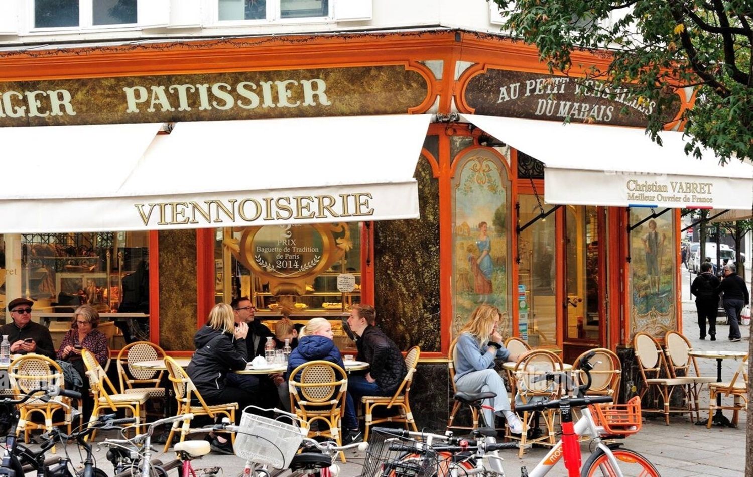 A café with outdoor seating, a traditional Parisian sign, and a bicycle parked in front.