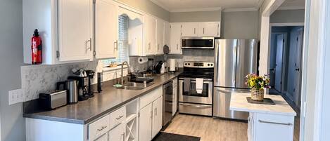 A modern kitchen with white cabinetry, stainless steel appliances, and a marble backsplash.
