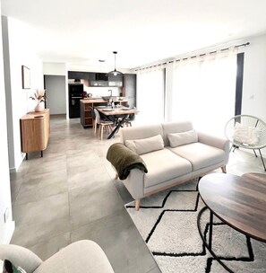 A modern living room with a sofa, a dining table, and a kitchen in the background.