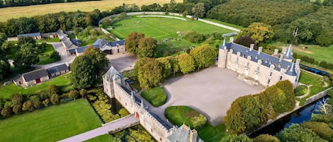 Luchtbeeld van een kasteel met een gracht, omgeven door weelderig groen en velden.